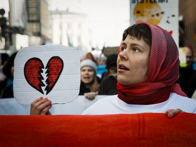 Frau auf Demo hält Plakat mit gebrochenem Herzen