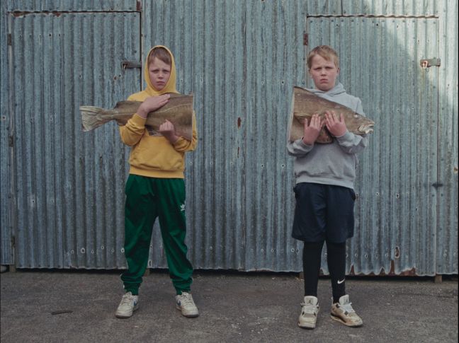 Die zwei Jungs halten einen Fisch, der eine den Schwanz, der andere den Kopf