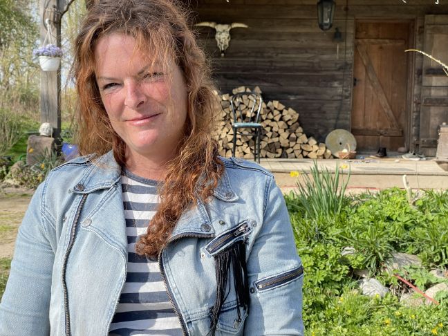 eine Frau im Garten vor einem Holzhaus mit einem Holzstapel davor
