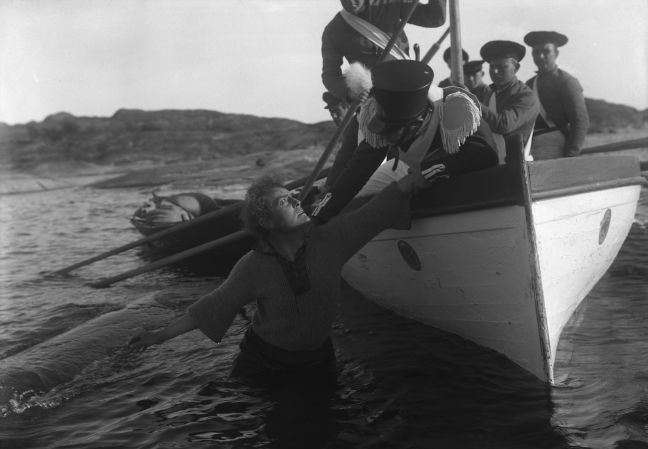 Terje Vigen steht im Wasser neben einem vollbesetzten Boot und blickt nach oben