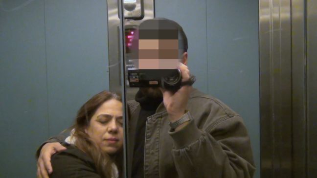 ein Mann mit einer Kamera und verpixeltem Gesicht und eine Frau im Fahrstuhlspiegel