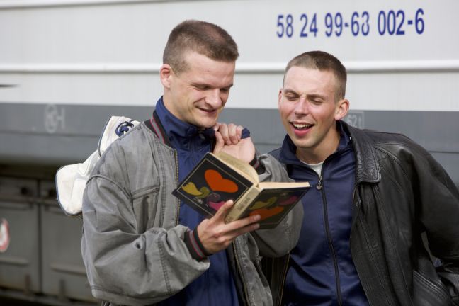 Zwei junge Männer stehen mit einem Buch am Bahnhof