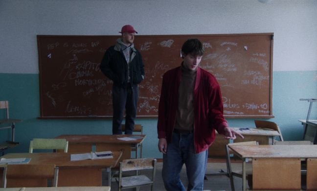 Domas steht auf einem Klassenstuhl und Ignas geht durch den Klassenraum