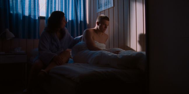 Emil sitzt im Bett, seine Mutter legt ihre Hand auf seinen Rücken