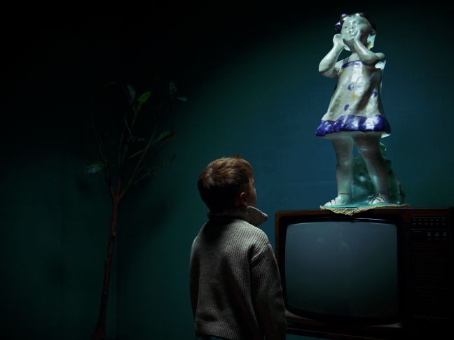 ein Junge betrachtet eine Figur die auf einem Fernseher steht
