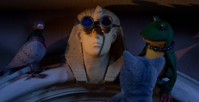 Frosch, Taube und Katze stehen um die Sphinx herum, die ein Fernglas hat