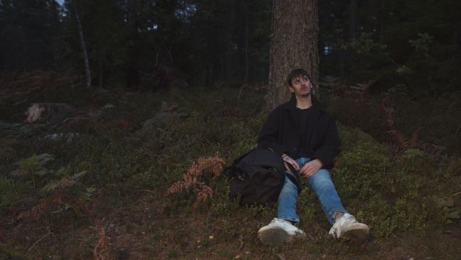August im Wald an einen Baumstamm gelehnt sitzend