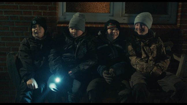 vier Kinder im Dunkeln mit einer Taschenlampe auf einer Bank vor einem Haus