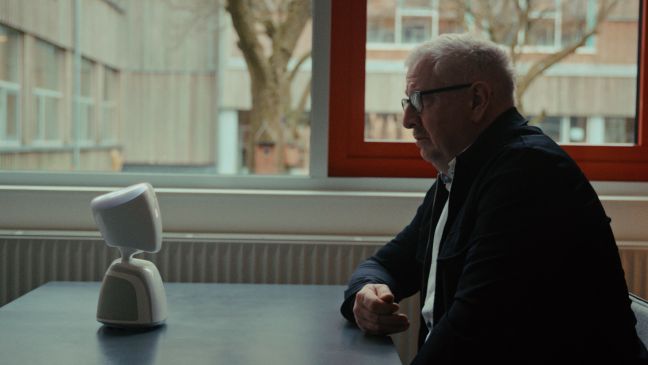 ein älterer Mann mit Lauras Telepräsenzroboter am Tisch