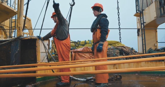 Zwei Menschen der Besatzung stehen an Deck mit oranger Arbeitskleidung