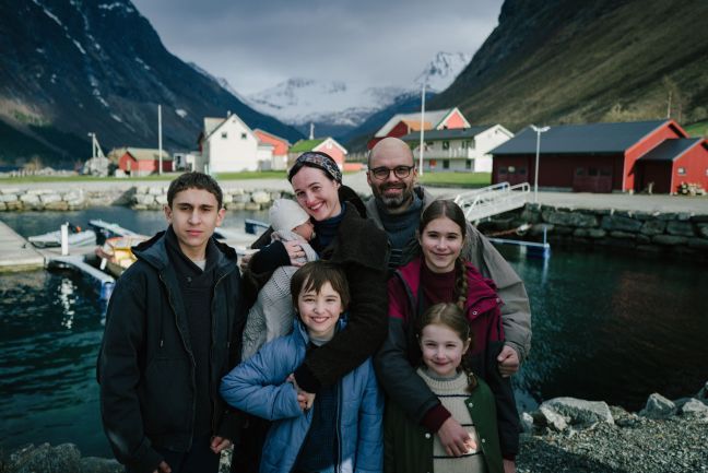 Die Familie steht vor der Küstenlandschaft am Fjord und lächelt in die Kamera